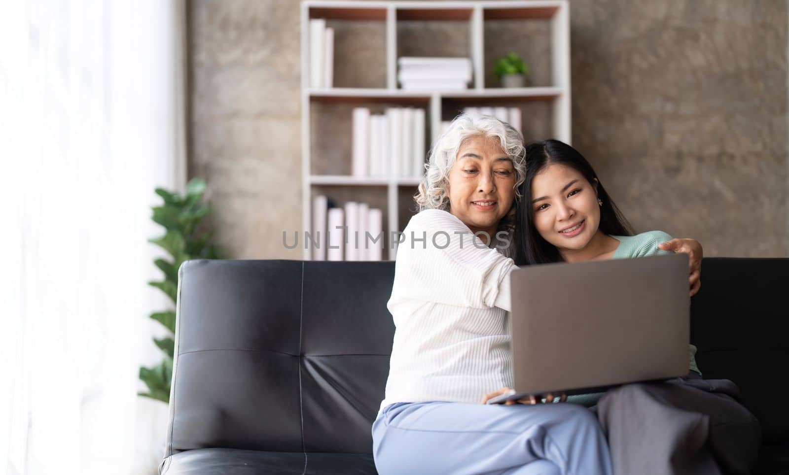 Mother up daughter sit on couch in living room hold on laptop looking at screen watching movie film, using device make video call, shopping website, daughter teach mom concept.