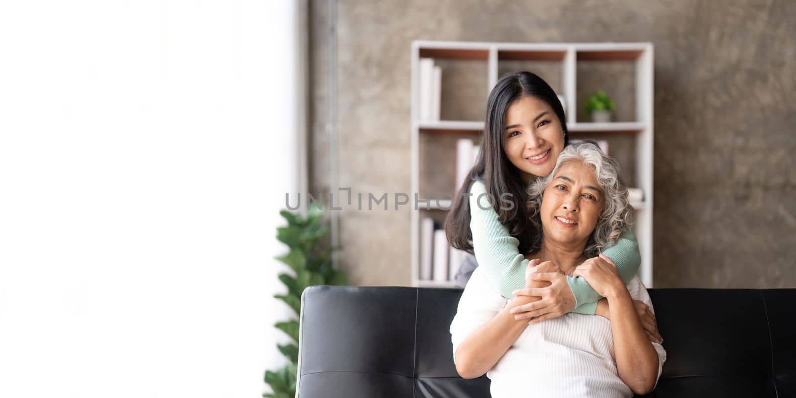 Happy daughter and mother having fun in living room, smiling mother hugging young grown daughter bonding chatting relaxing at home together by nateemee
