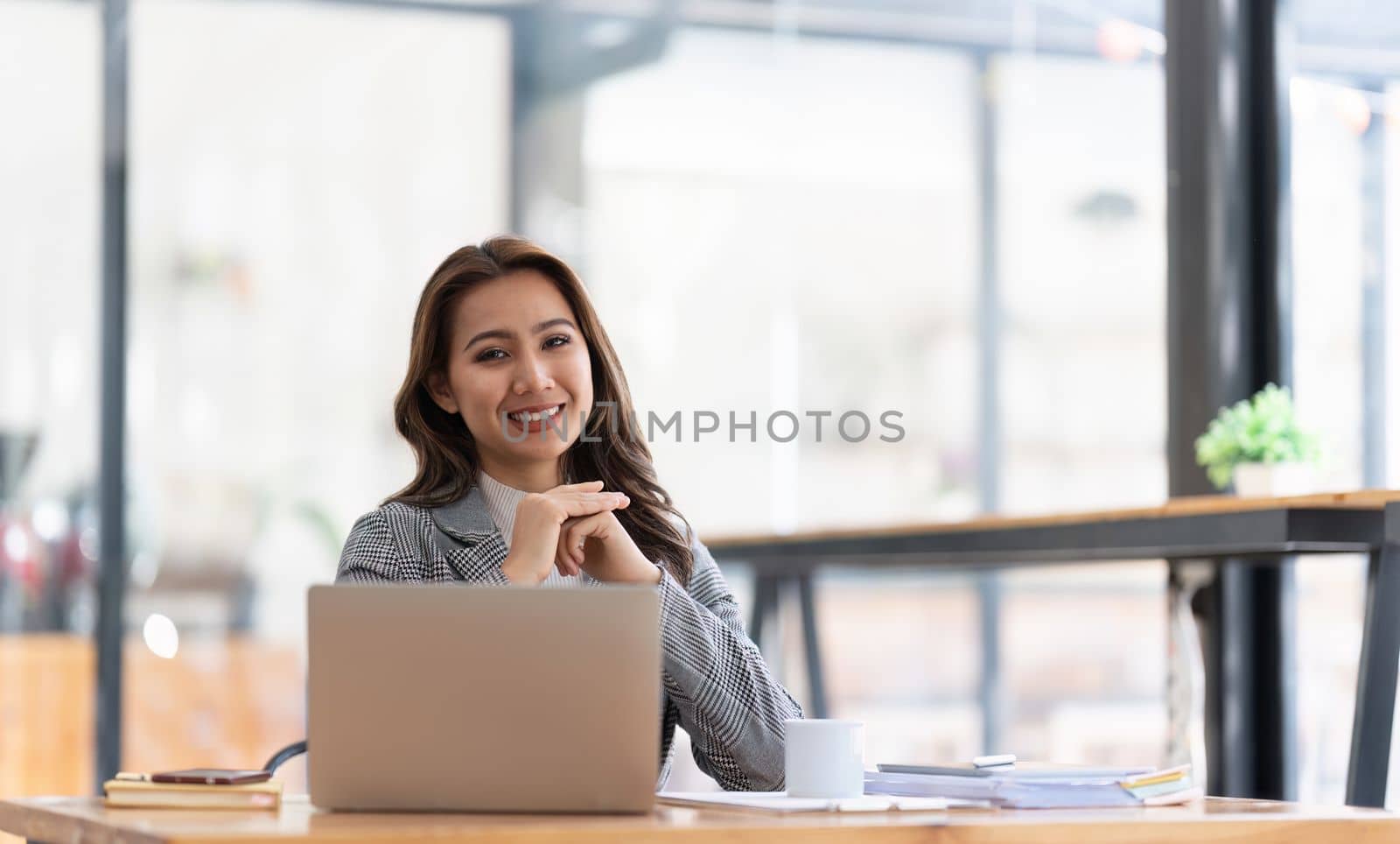 Young businesswoman working at her laptop and going over paperwork while sitting at a desk in an office by nateemee