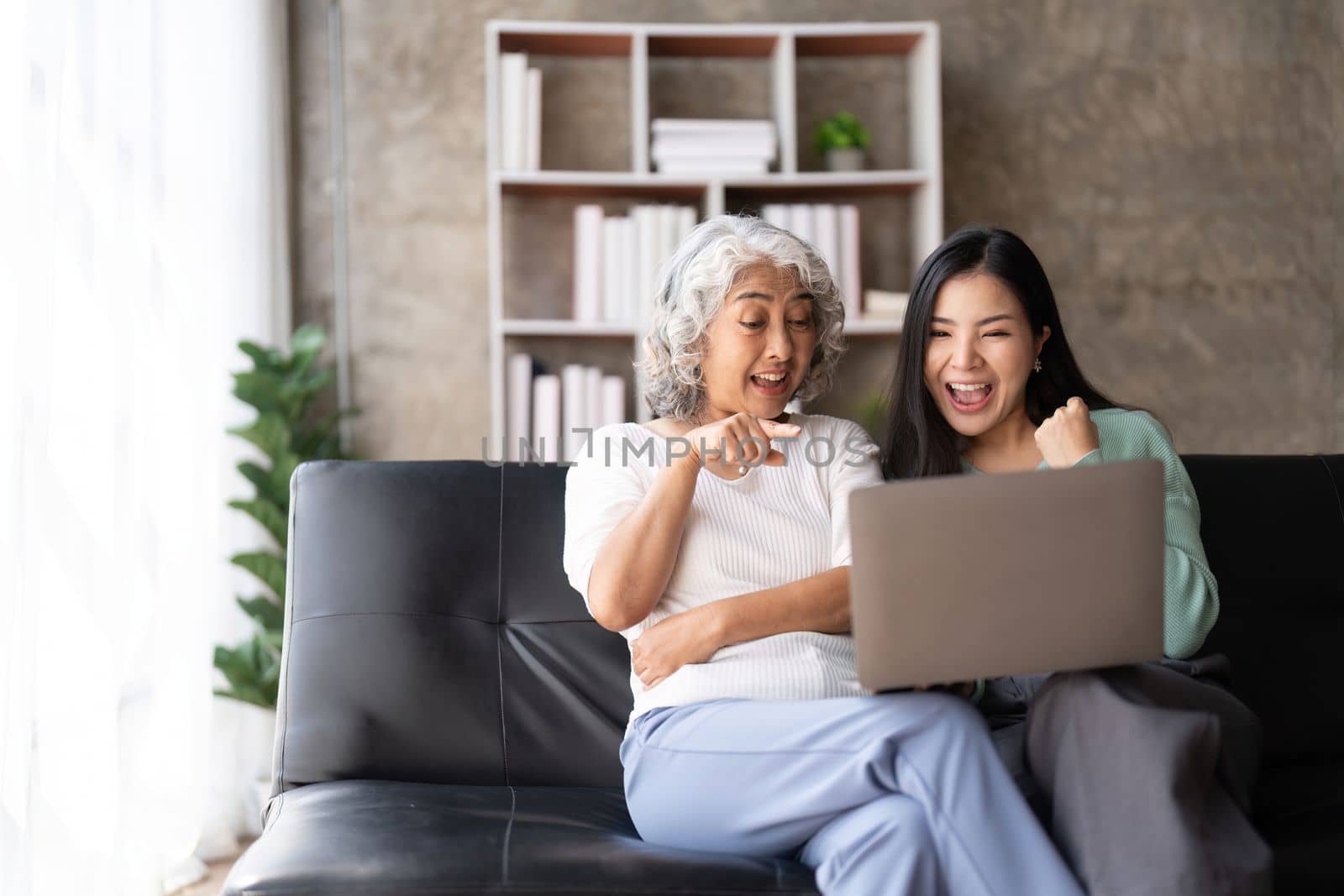 Mother up daughter sit on couch in living room hold on laptop looking at screen watching movie film, using device make video call, shopping website, daughter teach mom concept.