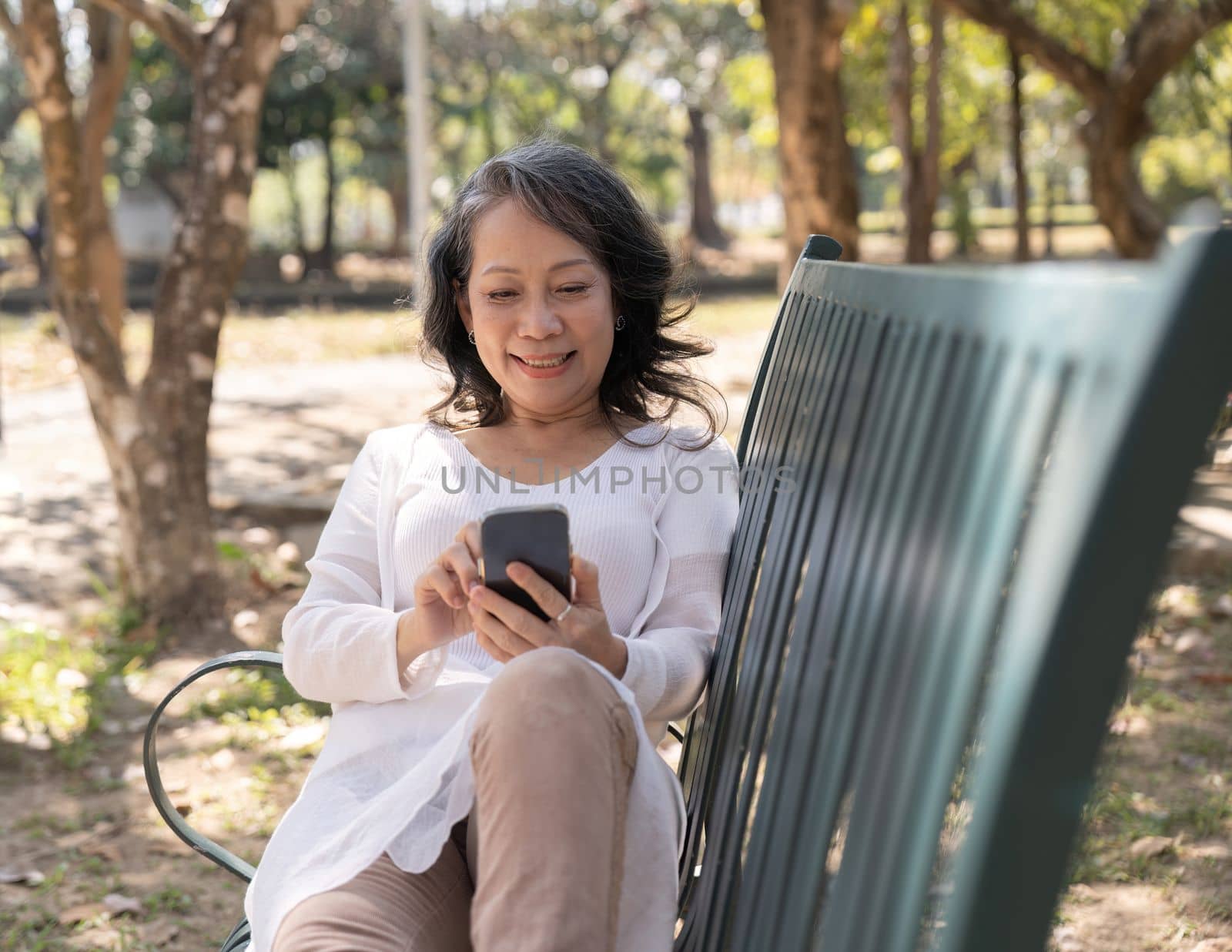 Aged woman using her smartphone while relaxing in the park.