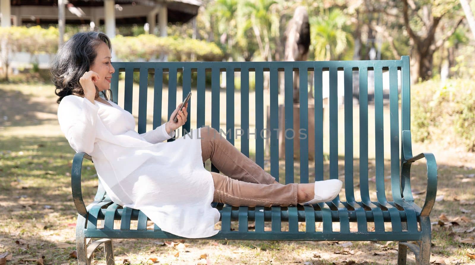 Aged woman using her smartphone while relaxing in the park.