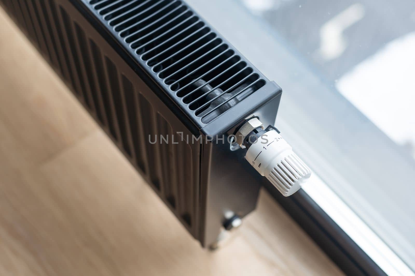 Detail of a modern black radiator under the window of a kitchen.