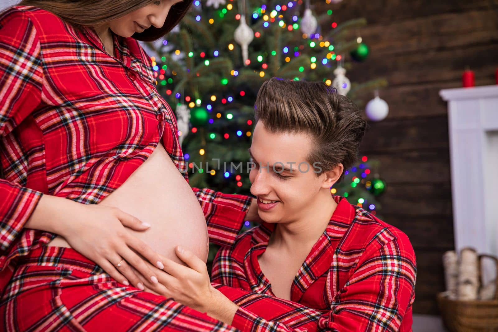 Close-up on the profile of a seated woman in advanced pregnancy. Partner smiling looks at pregnant belly and places hand on it. The woman looks down at her belly and holds her hand on it.