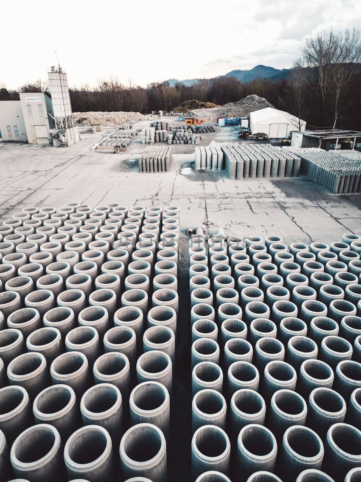 Vertical photo of construction company firm storage place with concrete pipes neatly lined up in rows on the grounds by VisualProductions