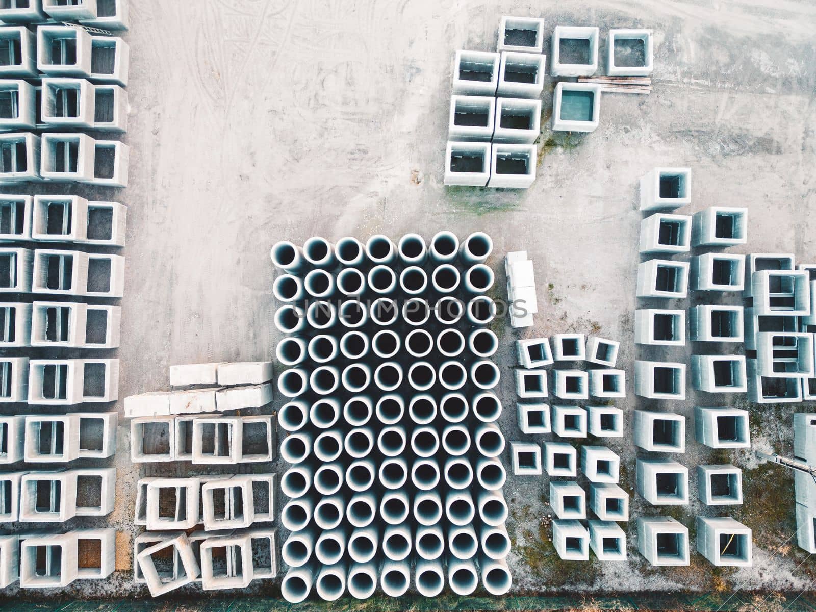 Looking down at concrete blocks and pipes neatly stacked in rows on the ground by VisualProductions