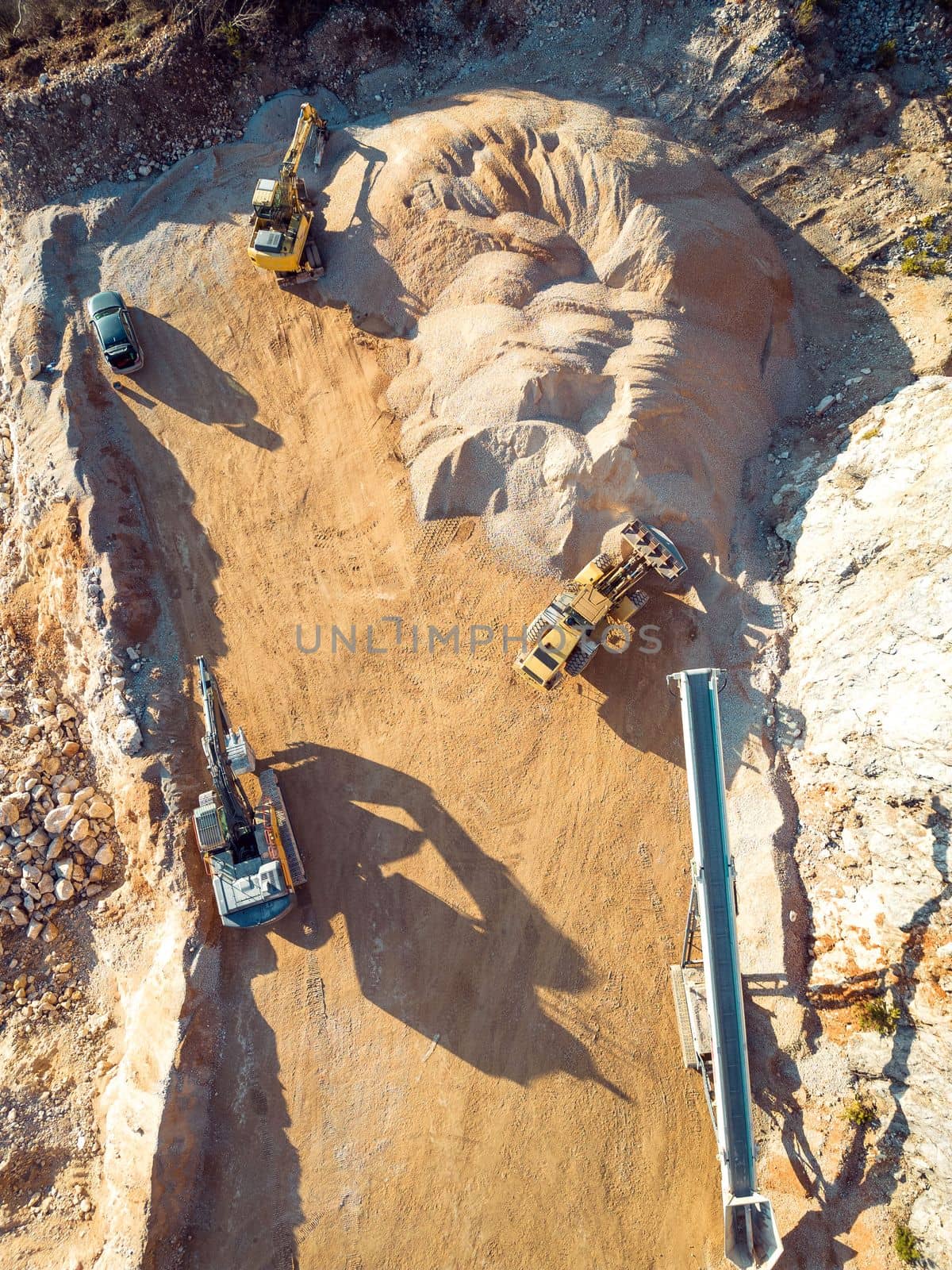 Vertical photo of yellow heavy machinery, excavators working on dusty quarry grounds by VisualProductions