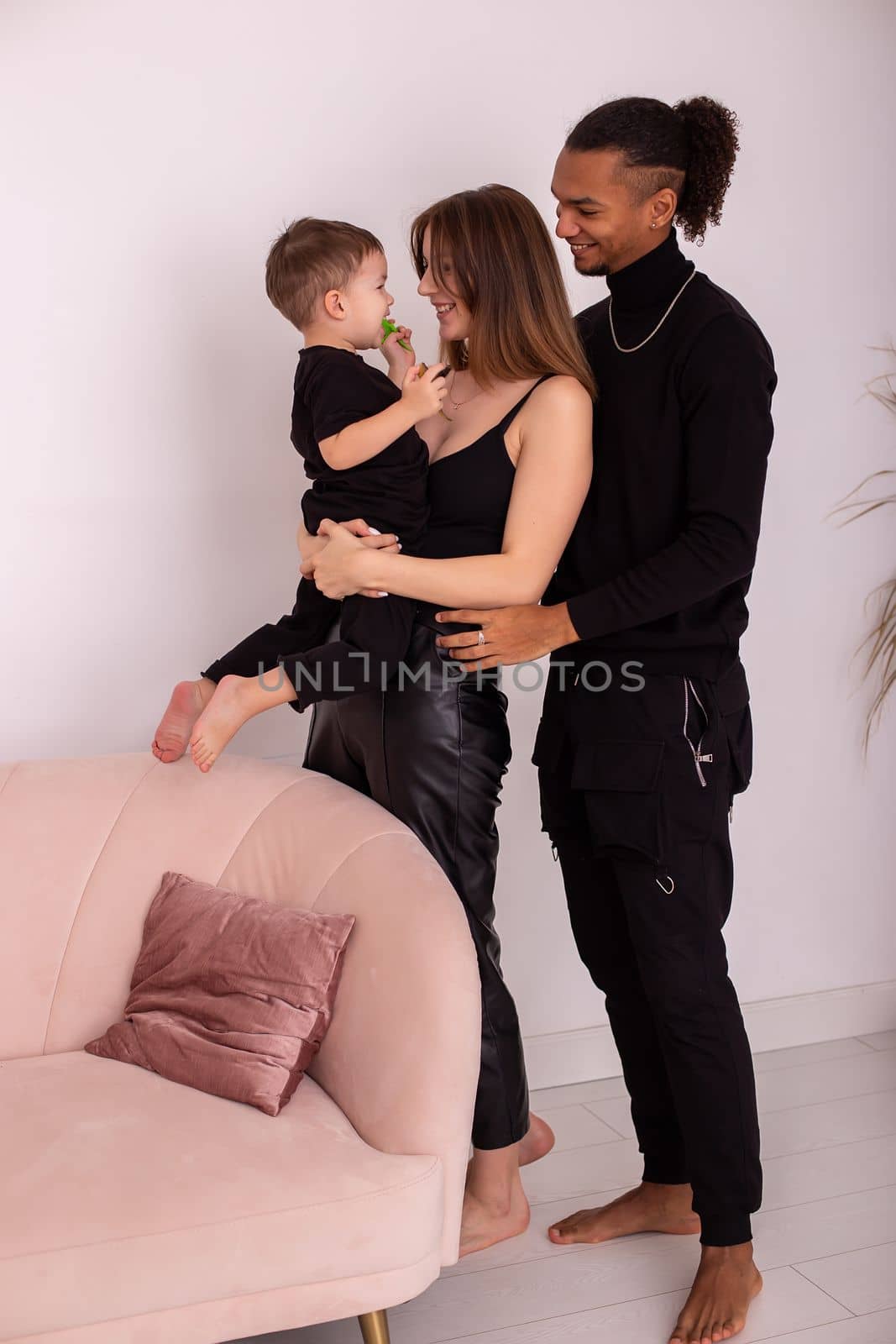 A happy multiracial family. A mother is holding a little boy, in black clothes, a stylish young man is standing next to her. Vertical . Copy space