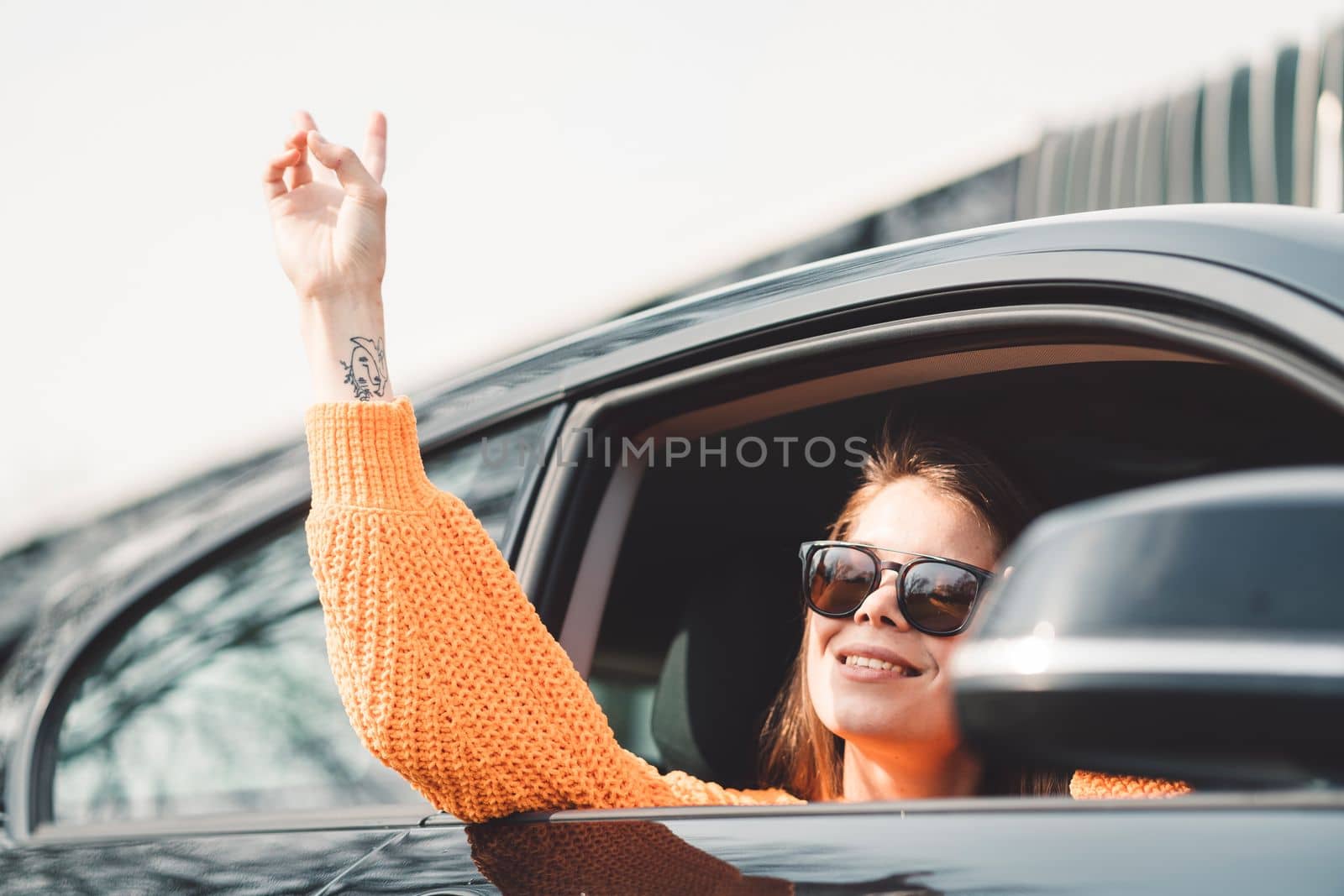 Beautiful young happy smiling caucasian woman driving in her car, wearing sunglasses and an orange sweater. High quality photo