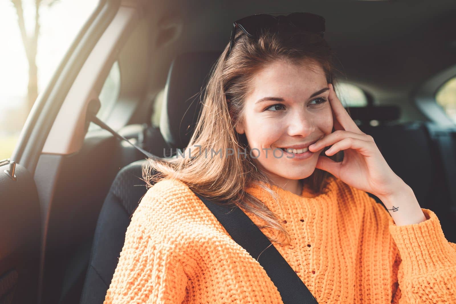 Beautiful young happy smiling caucasian woman driving in her car, wearing sunglasses and an orange sweater. High quality photo