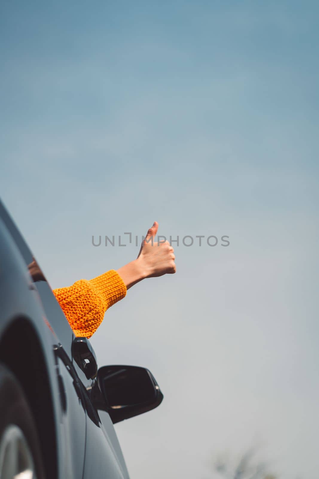 Vertical photo of persons hand sticking out the car window holding thumbs up by VisualProductions