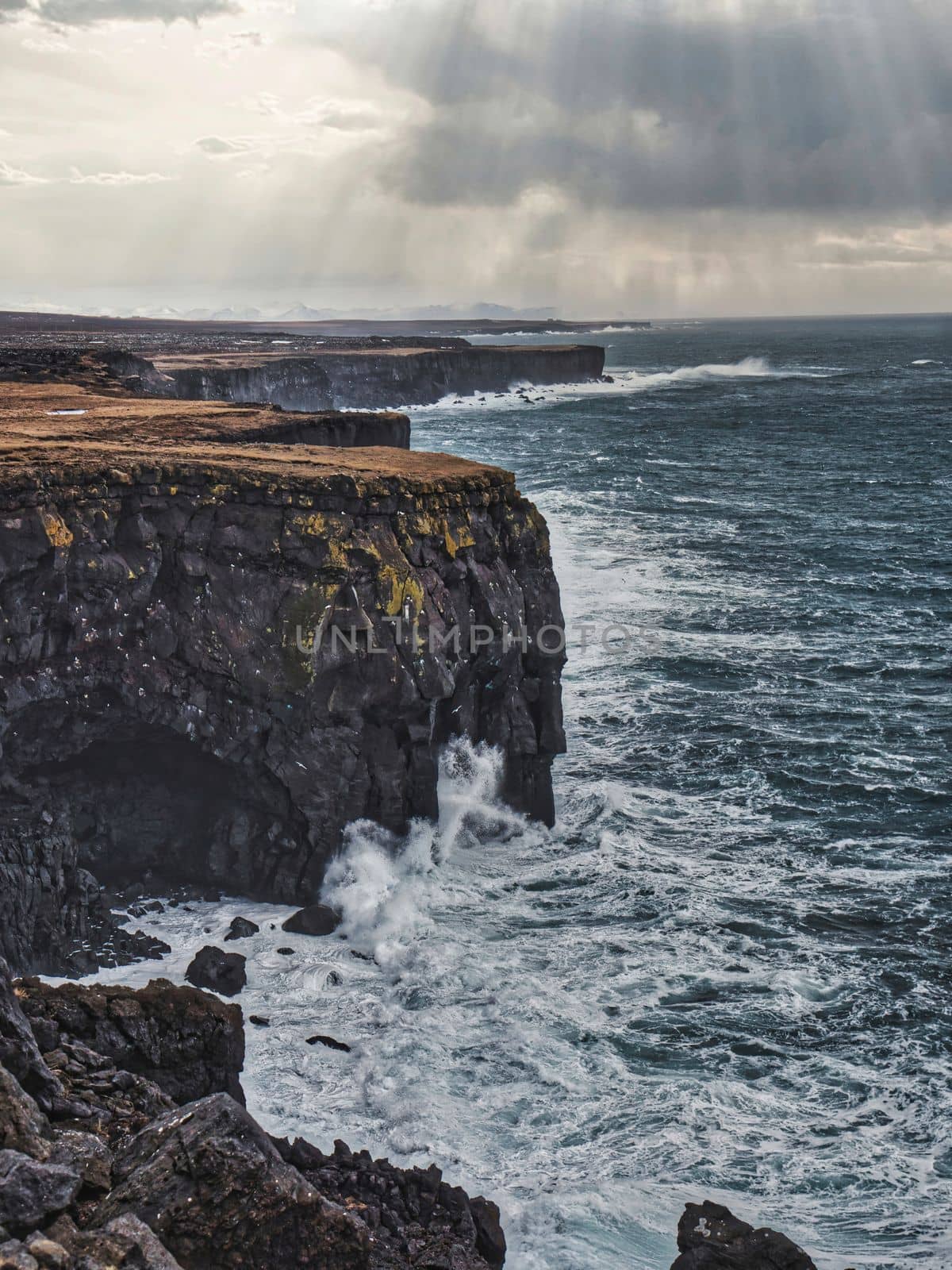 Cold sea water crashing against rocks near rough stony cliffs, on stormy day in Iceland