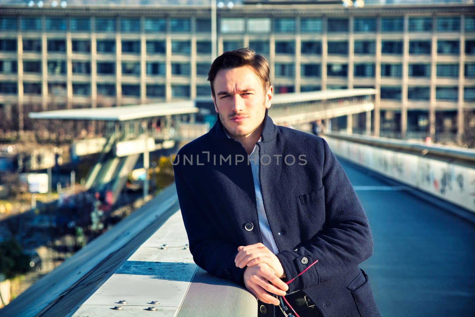 One handsome elegant young man in urban setting in city, standing, looking at camera wearing coat