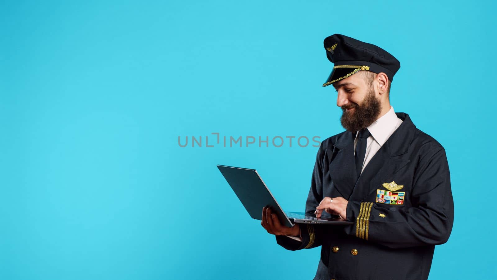 Modern aircrew captain using laptop on camera, browsing online website and social media app. Male pilot working on commercial flights and holding wireless computer, navigating internet.