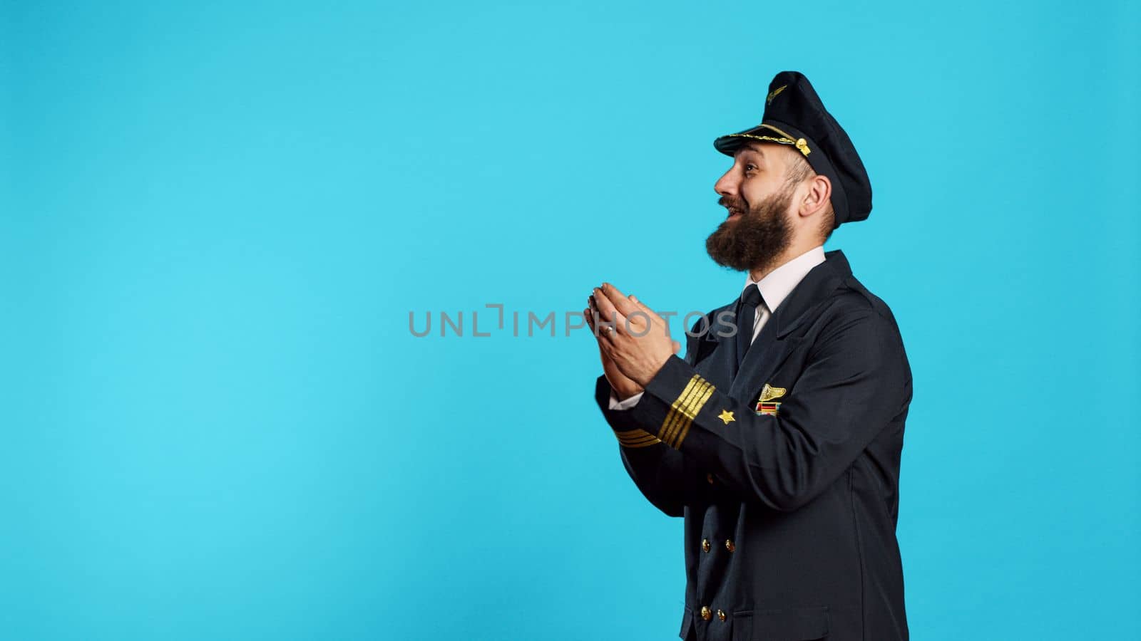 Male aviator applauding and cheering on camera, saying congratulations and clapping hands in studio. Airline pilot in flying uniform with cheerful emotions doing standing ovation sign.