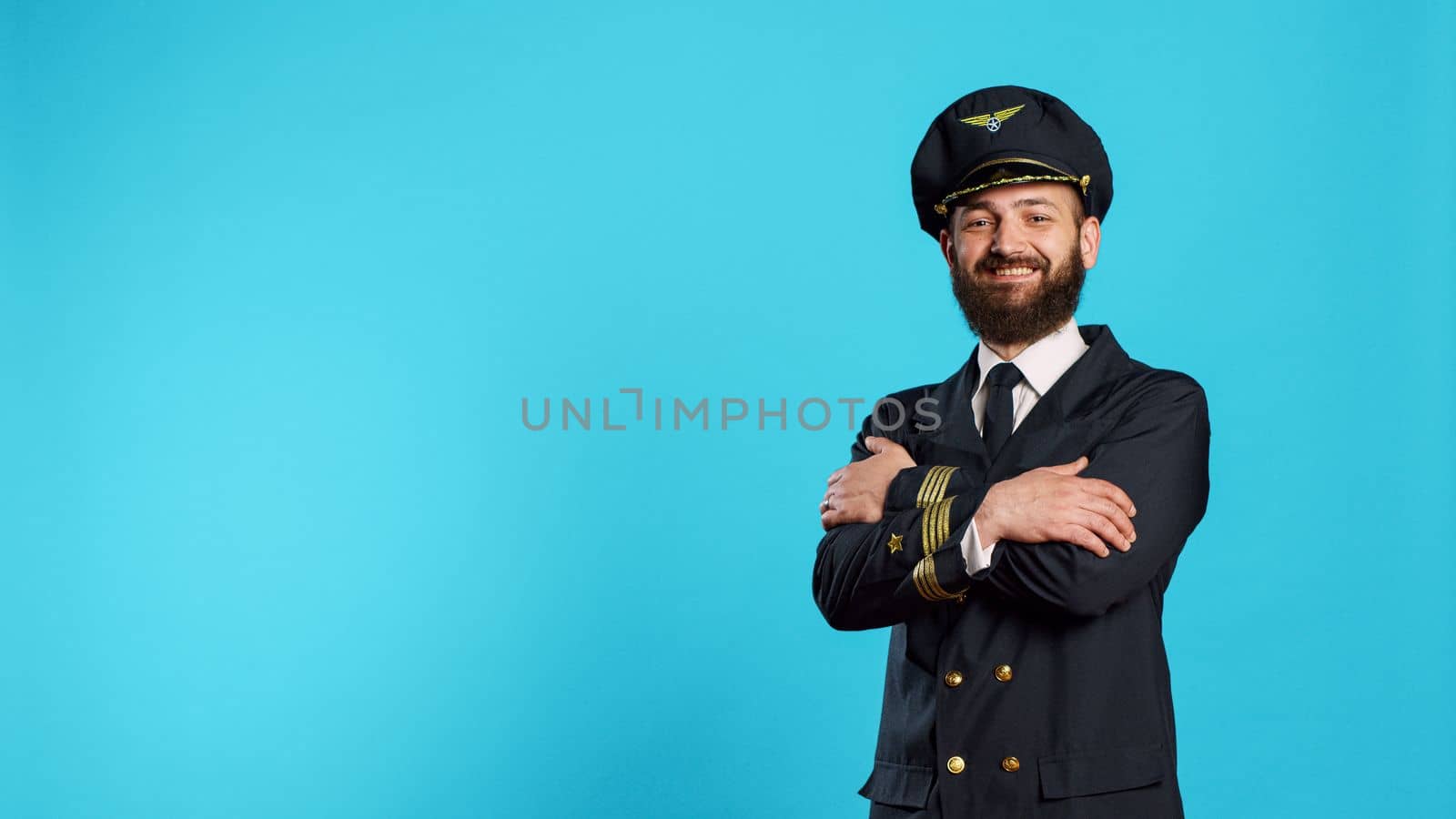 Portrait of smiling aircrew captain posing on camera, acting positive and confident with aviation uniform. Male pilot having professional occupation for air transport, flying airplane.