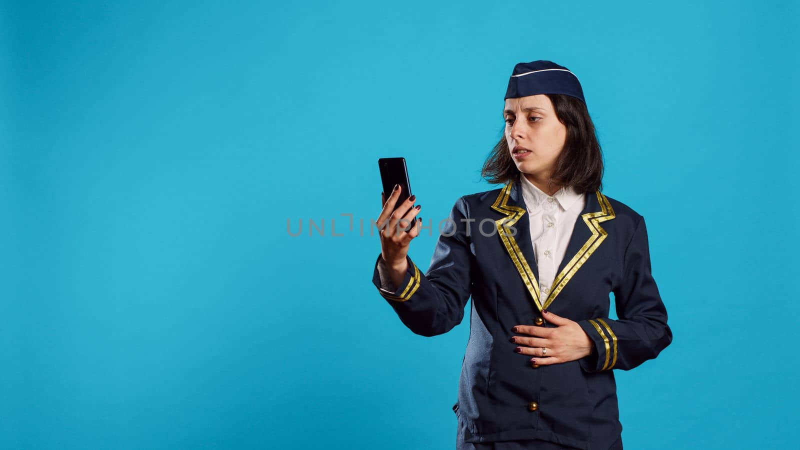Air hostess attending online video call conference on smartphone, chatting on internet videoconference with webcam on camera. Young smiling stewardess talking on teleconference chat.