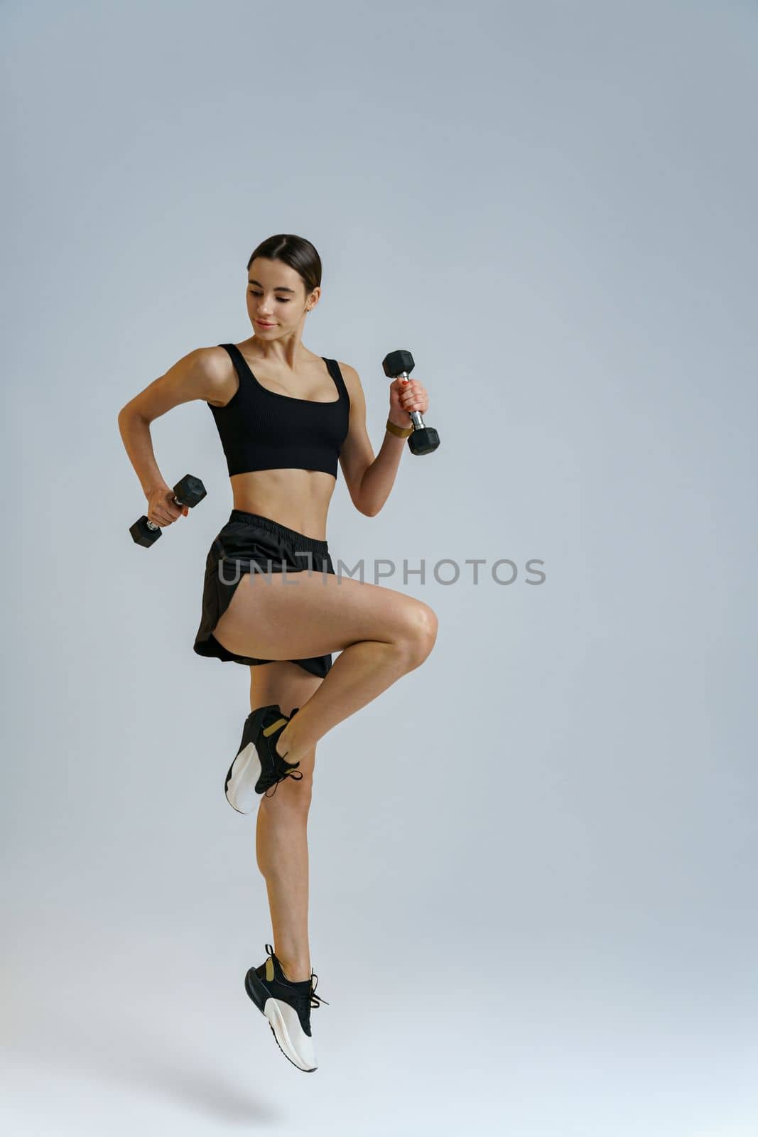 Fitness woman wearing sportswear doing cardio exercises with dumbbells on studio background by Yaroslav_astakhov