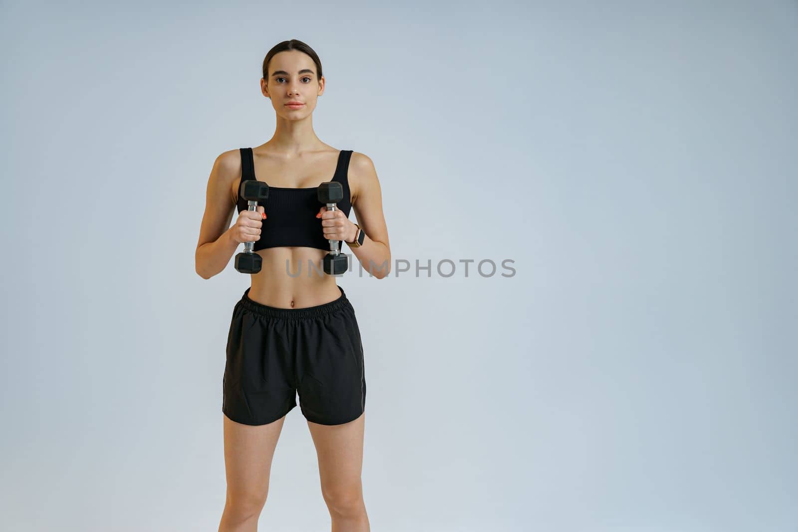 Attractive fitness woman doing exercises with dumbbells on studio background and looking at camera by Yaroslav_astakhov