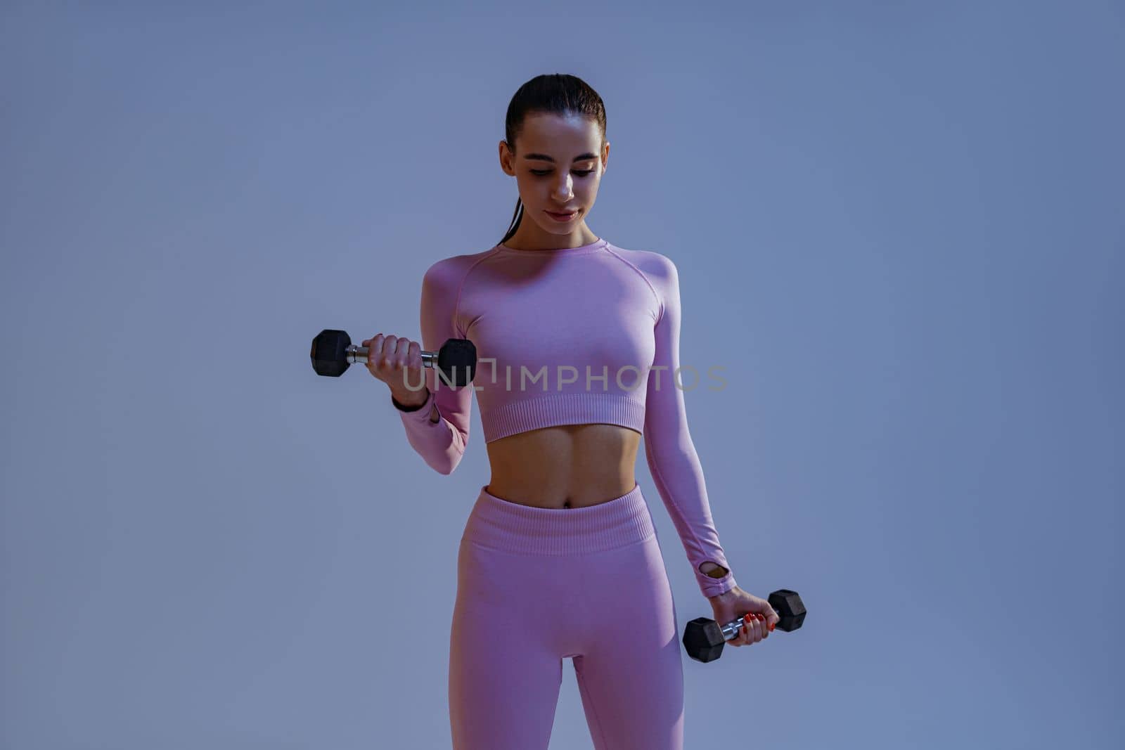 Fitness woman doing exercises with dumbbells on studio background. Strength and motivation by Yaroslav_astakhov