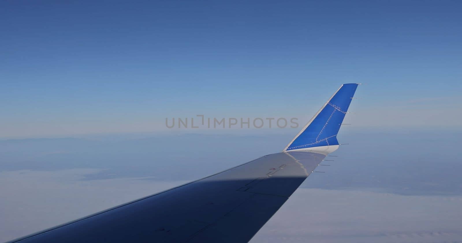 An airplane wing flying above clouds as seen through window against background of fluffy clouds