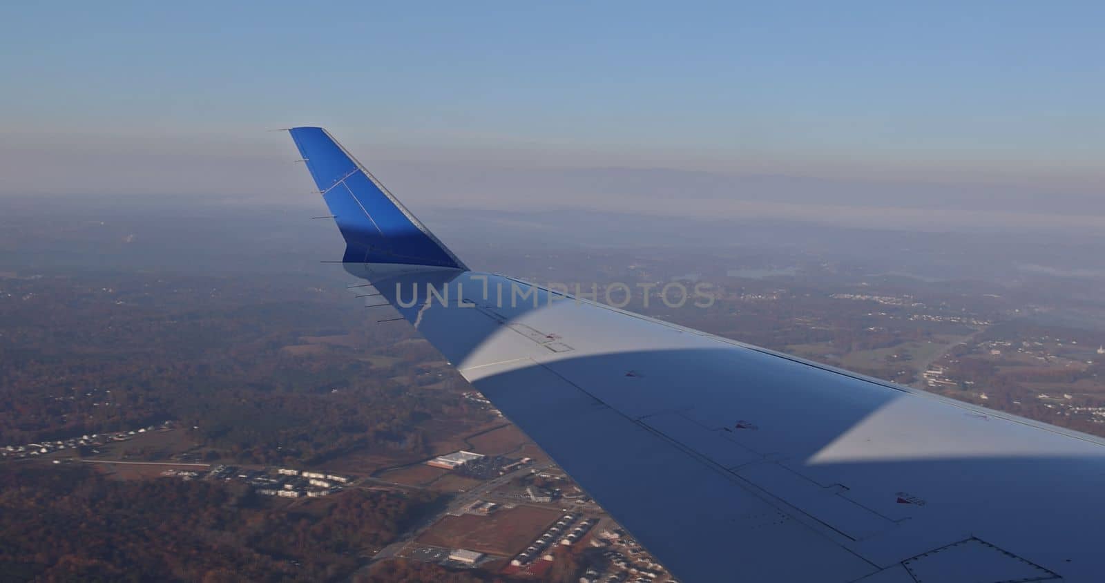 Airplane wing in view out a window with fluffy clouds in the sky backed by a background of earth by ungvar