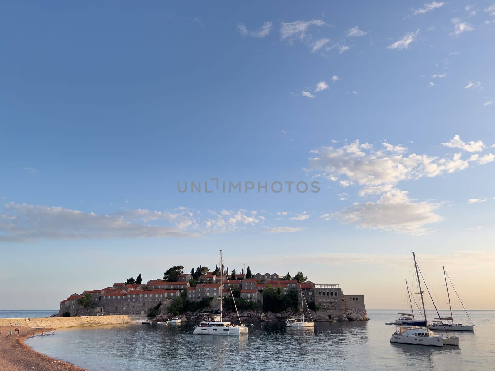 Sveti Stefan island with moored catamarans against a cloudy sky. High quality photo