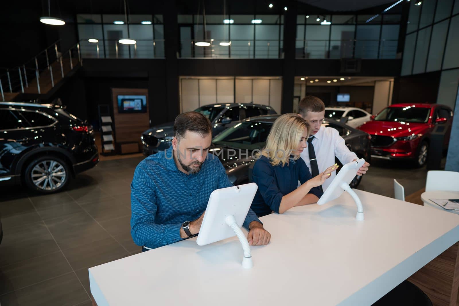 Caucasian married couple chooses a car in a car dealership on digital tablets