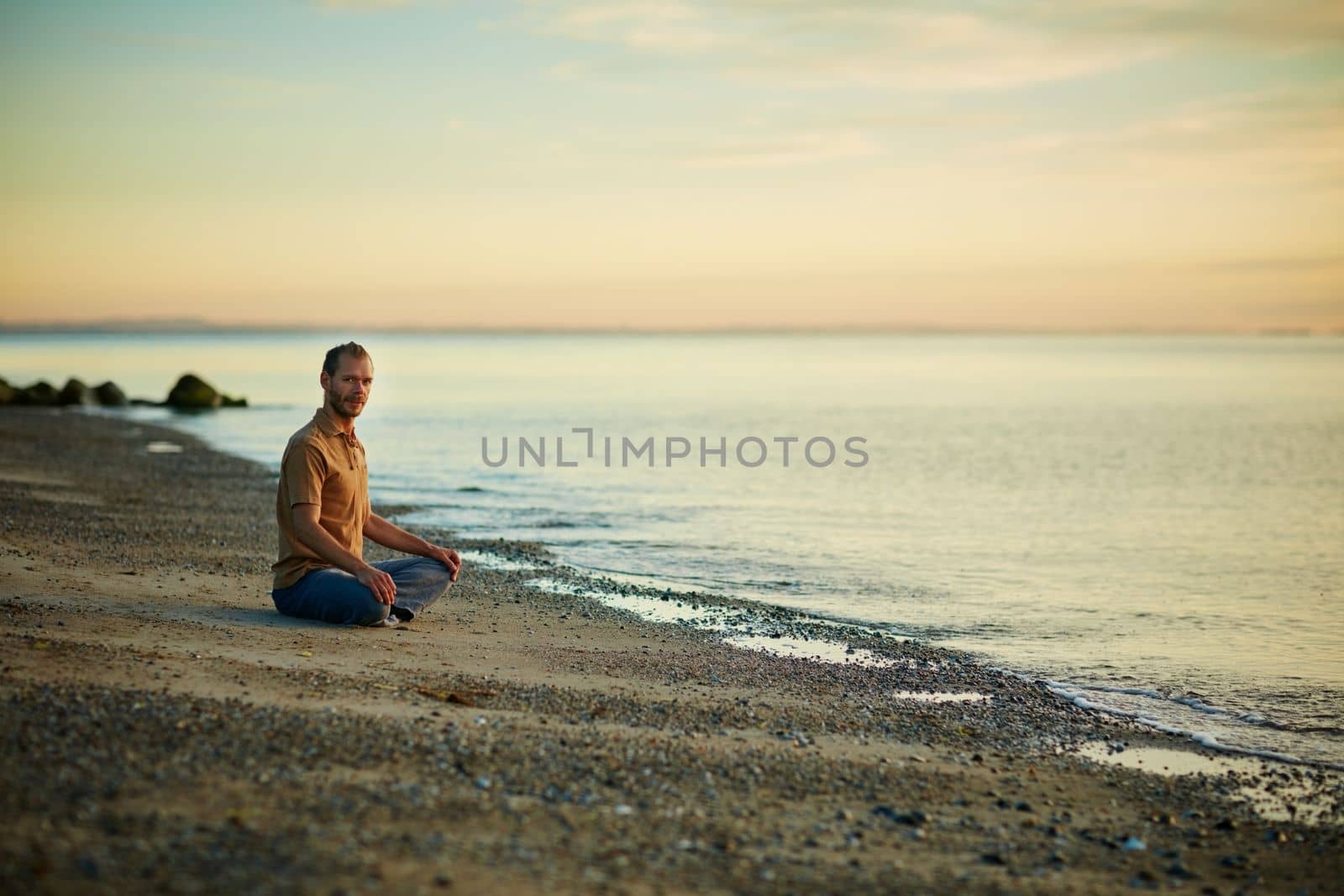 Yoga heals the soul. a man sitting in the lotus position during his yoga routine at the beach. by YuriArcurs