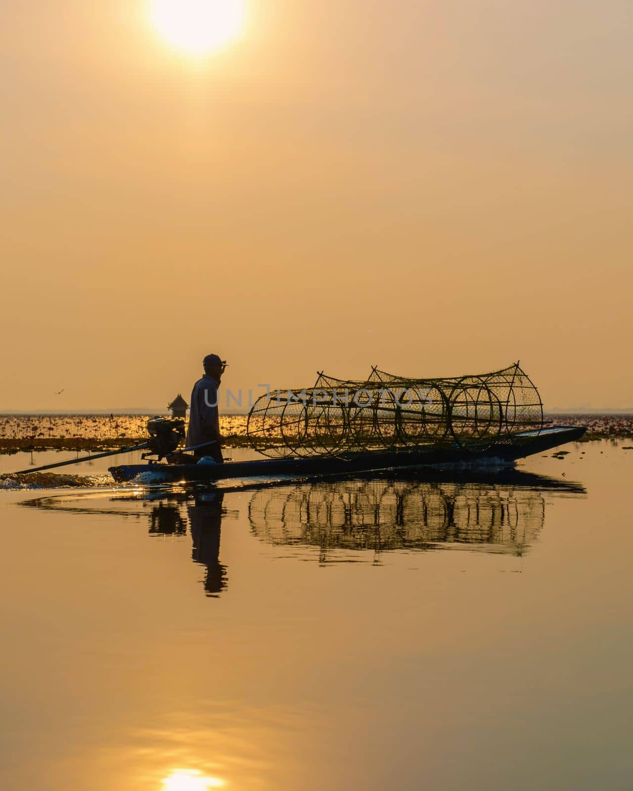 Fishermen in a boat at Sunrise at The sea of red lotus, Lake Nong Harn, Udon Thani, Thailand February 2023