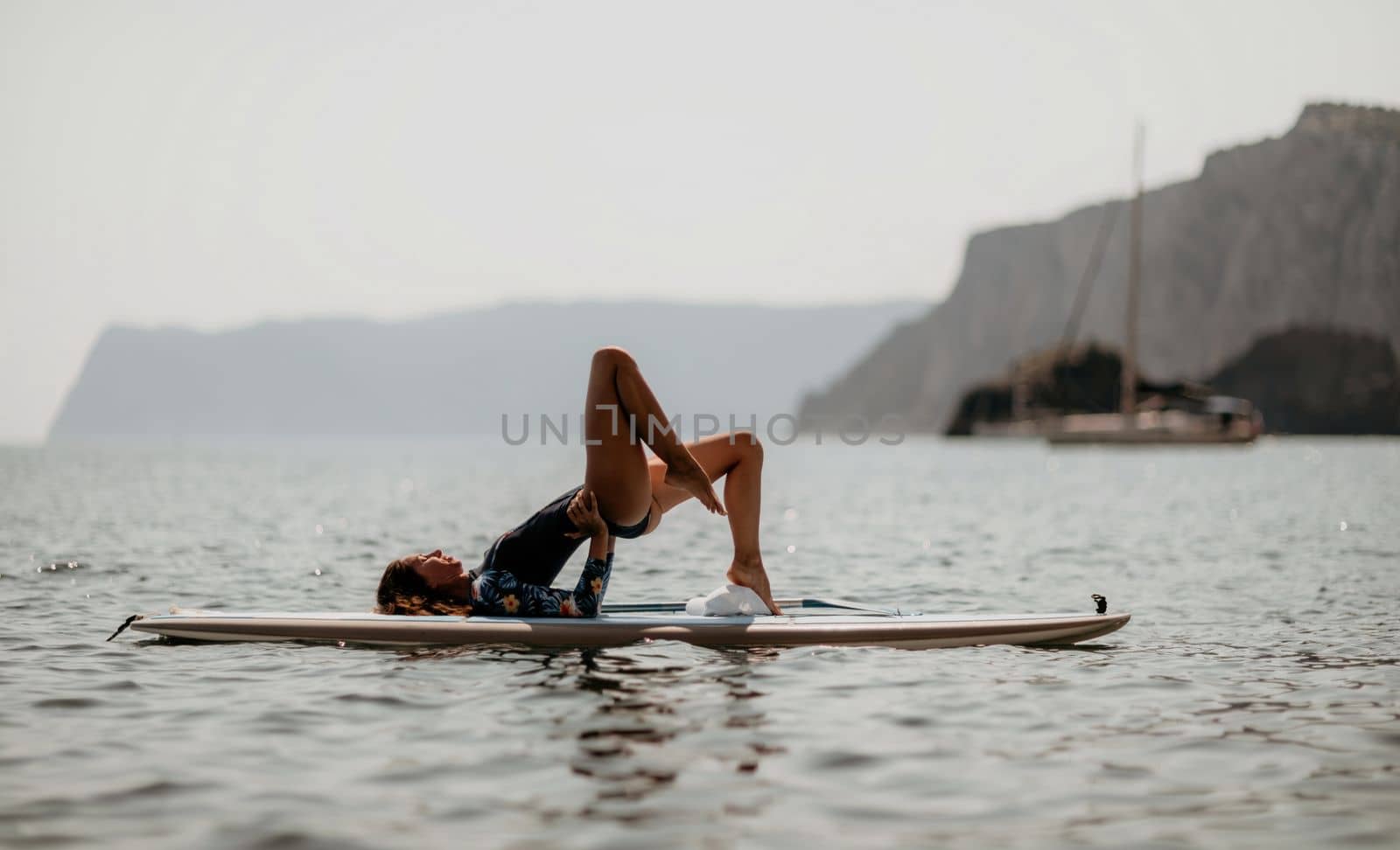 Woman sup yoga. Middle age sporty woman practising yoga pilates on paddle sup surfboard. Female stretching doing workout on sea water. Modern individual hipster outdoor summer sport activity