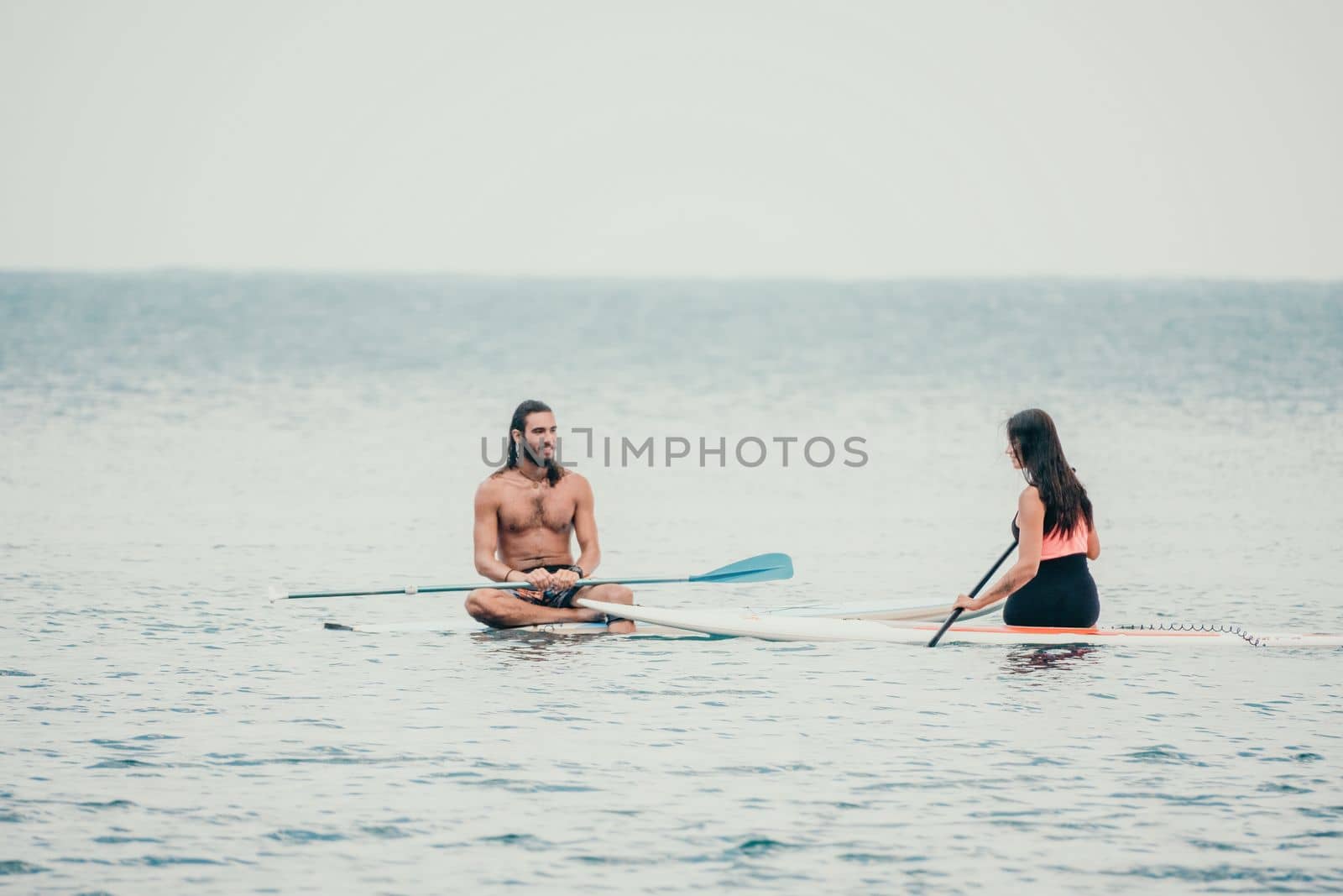 Sea woman and man on sup. Silhouette of happy young woman and man, surfing on SUP board, confident paddling through water surface. Idyllic sunset. Active lifestyle at sea or river