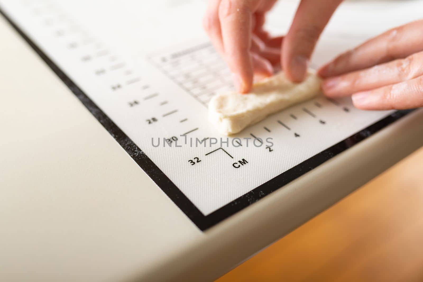 Close-up of hands measuring the length of a piece of dough on a kitchen mat with metric markings. Copy space.