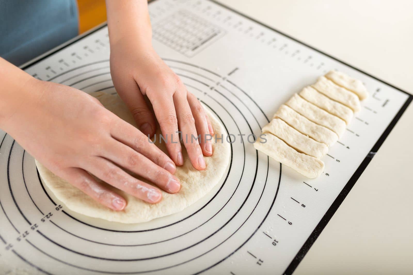 Close-up of hands kneading rolled out dough on a kitchen baking mat with round markings of different diameters.