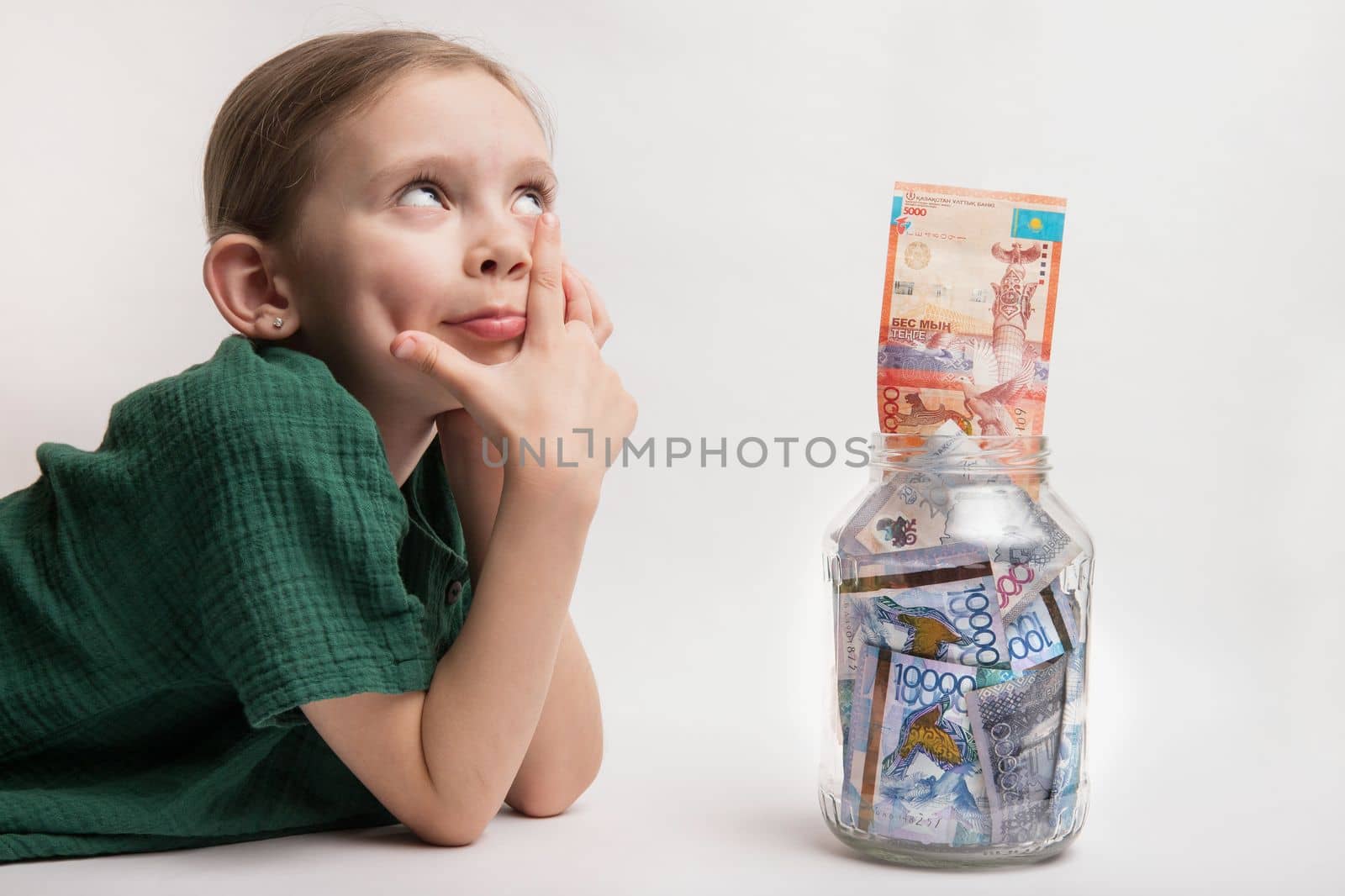 Happy girl with a large transparent jar with Kazakhstani tenge money. the child thought about new toys and gadgets.