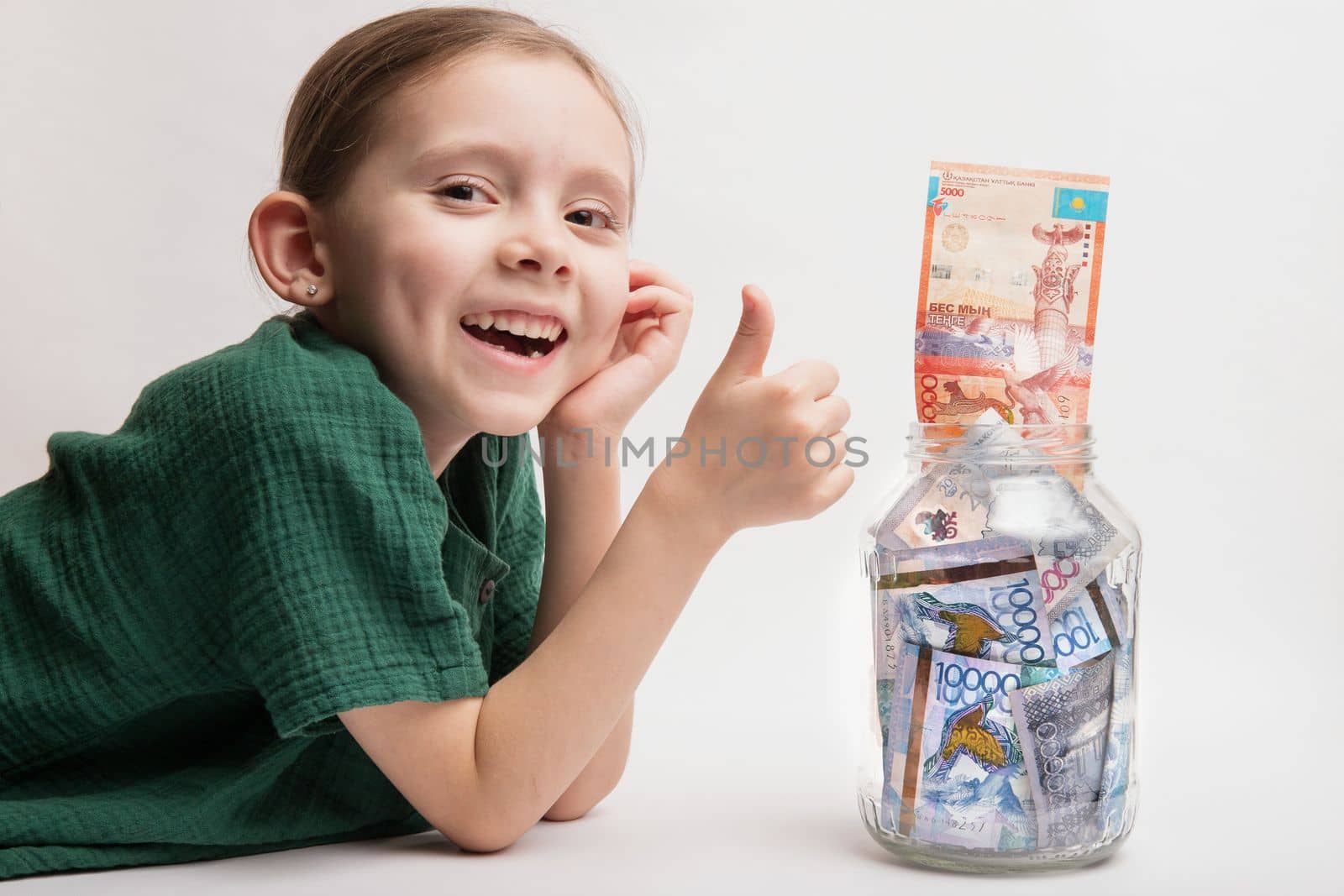Kid with a large transparent jar with Kazakhstani tenge money. Bank account for a child.