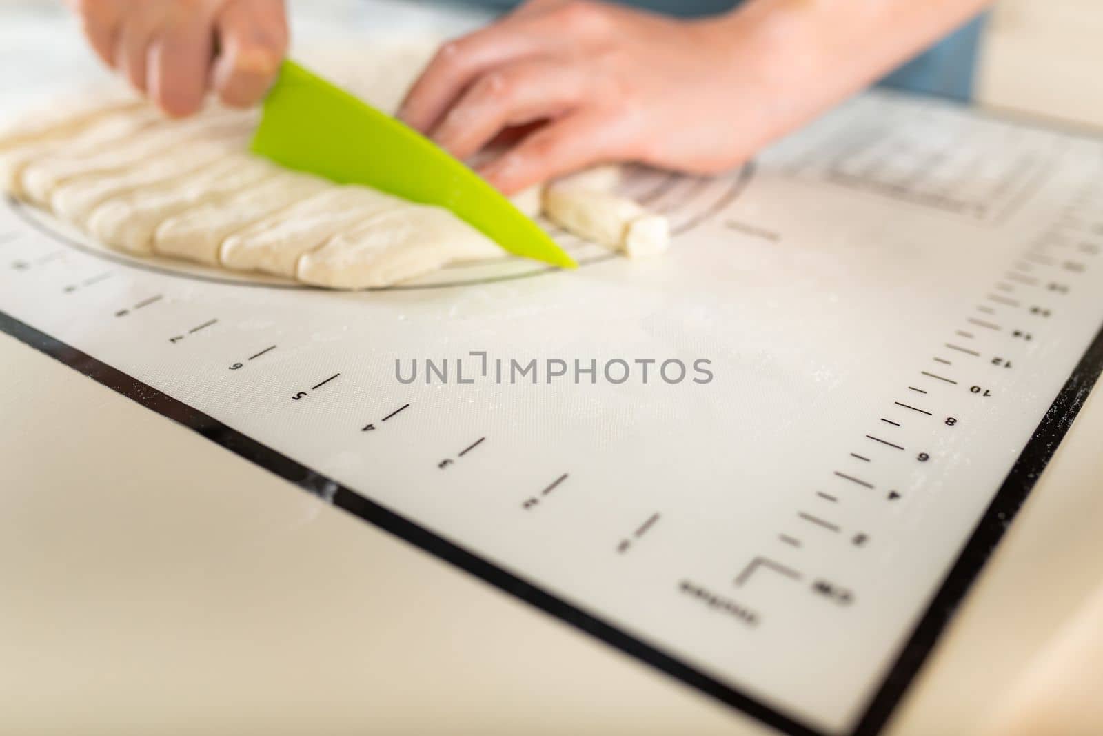 Close-up on cutting wheat dough on a kitchen mat with markings with a plastic knife on the cooking table, copy space.