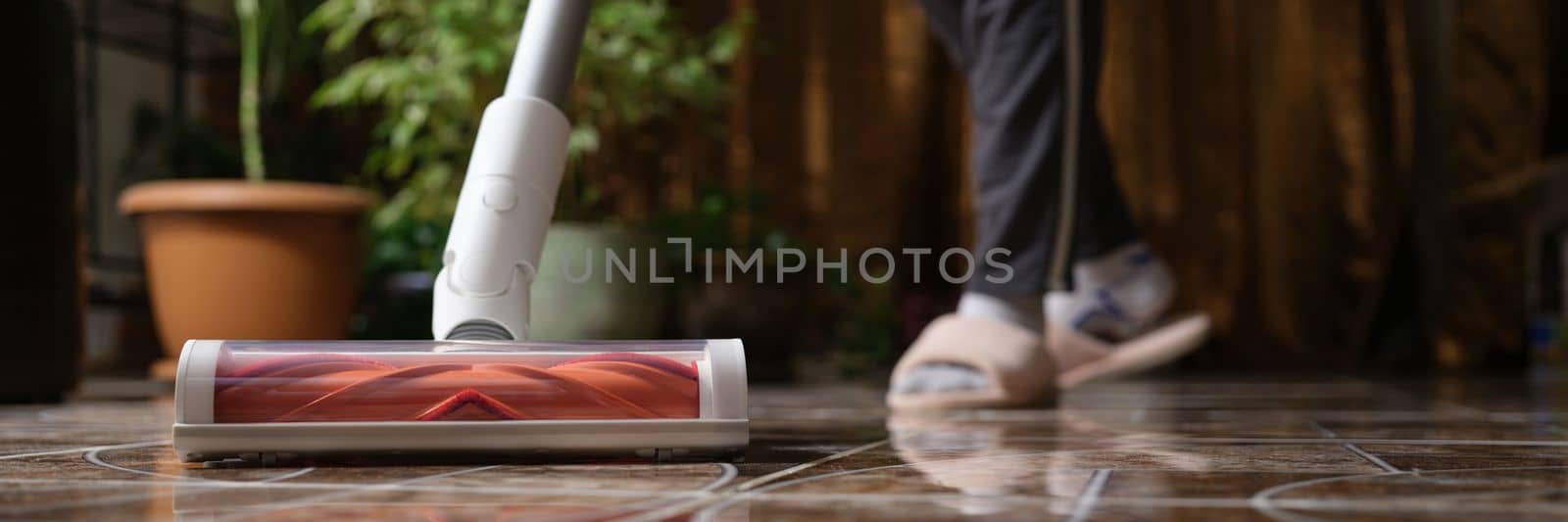 Cordless vacuum cleaner with turbo brush cleans tiles in living room. Modern home cleaning technology concept