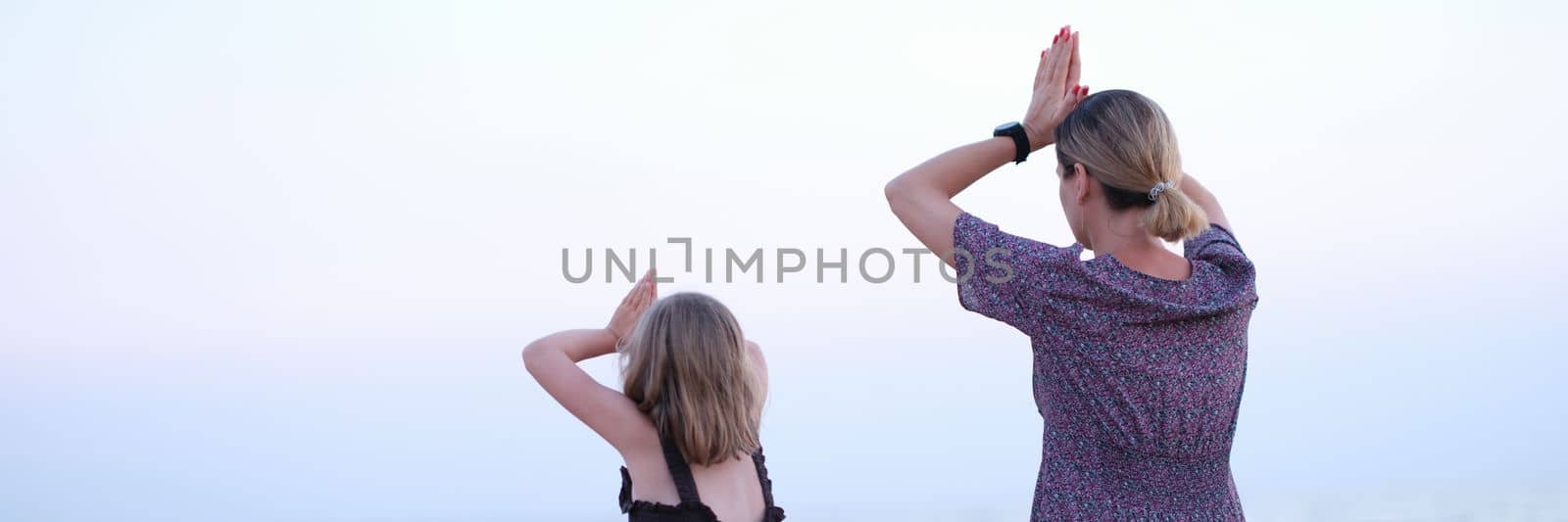 Mother and daughter do yoga meditate in lotus position on beach. Family yoga class by sea concept
