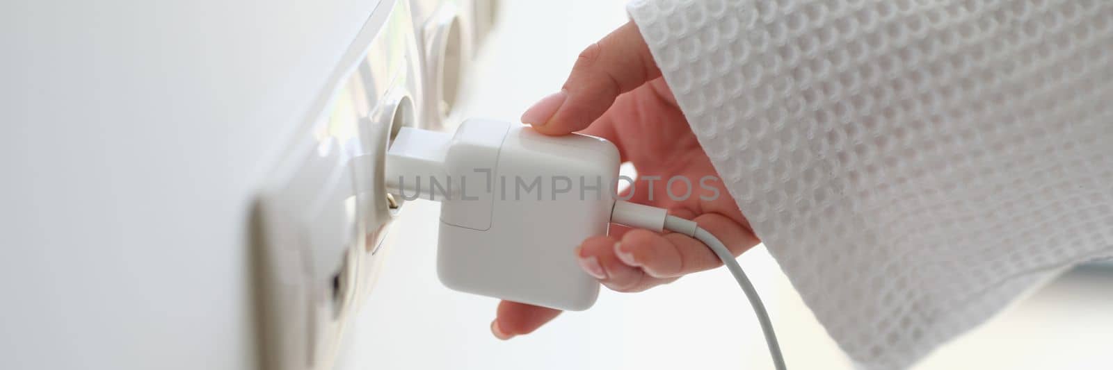 Woman hand in robe gown inserts white charger into socket in hotel rooms or at home by kuprevich