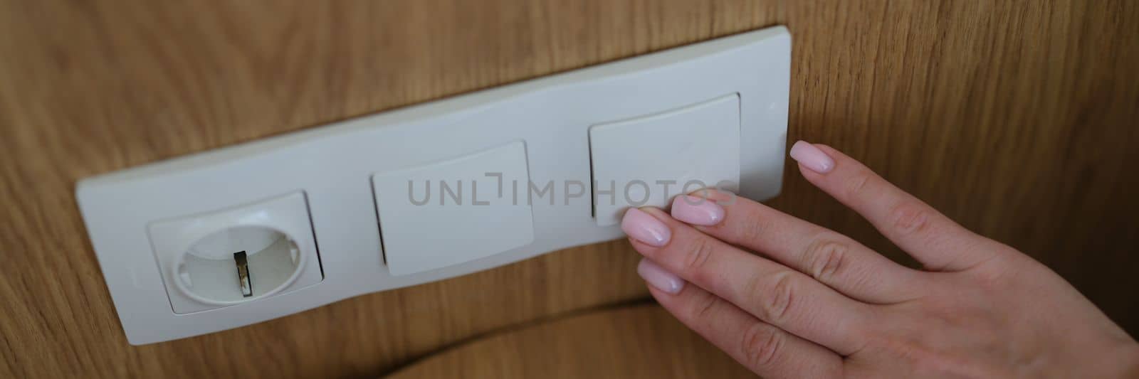 Woman hand presses on turn off lights closeup. Electric socket with plug and smartphone concept