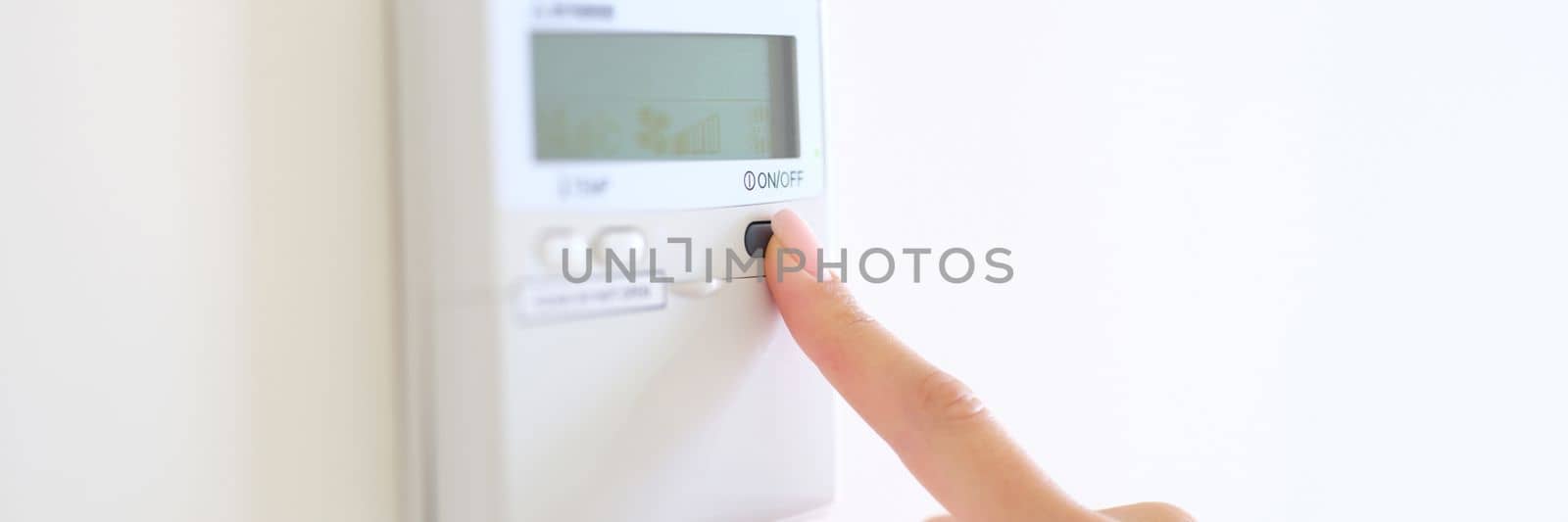 Wall mounted digital climate control and home thermostat. Female fingers set comfortable degrees of temperature adjustment in living room or hotel closeup