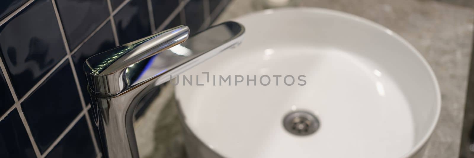 Washbasin and bathroom faucet detail of room interior. Chrome faucet and round porcelain washbasin concept