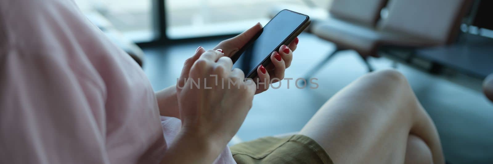 Woman traveler with smartphone in her hands sits in departure area at airport or train station by kuprevich