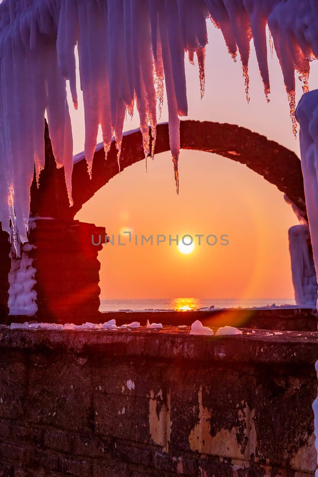 Winter sea view of a frozen fence and sun between ice window. Vertical view