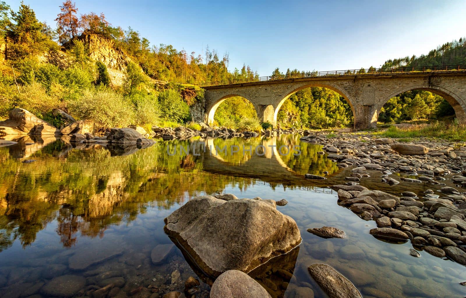 peaceful river with water reflection and old stone bridge	
