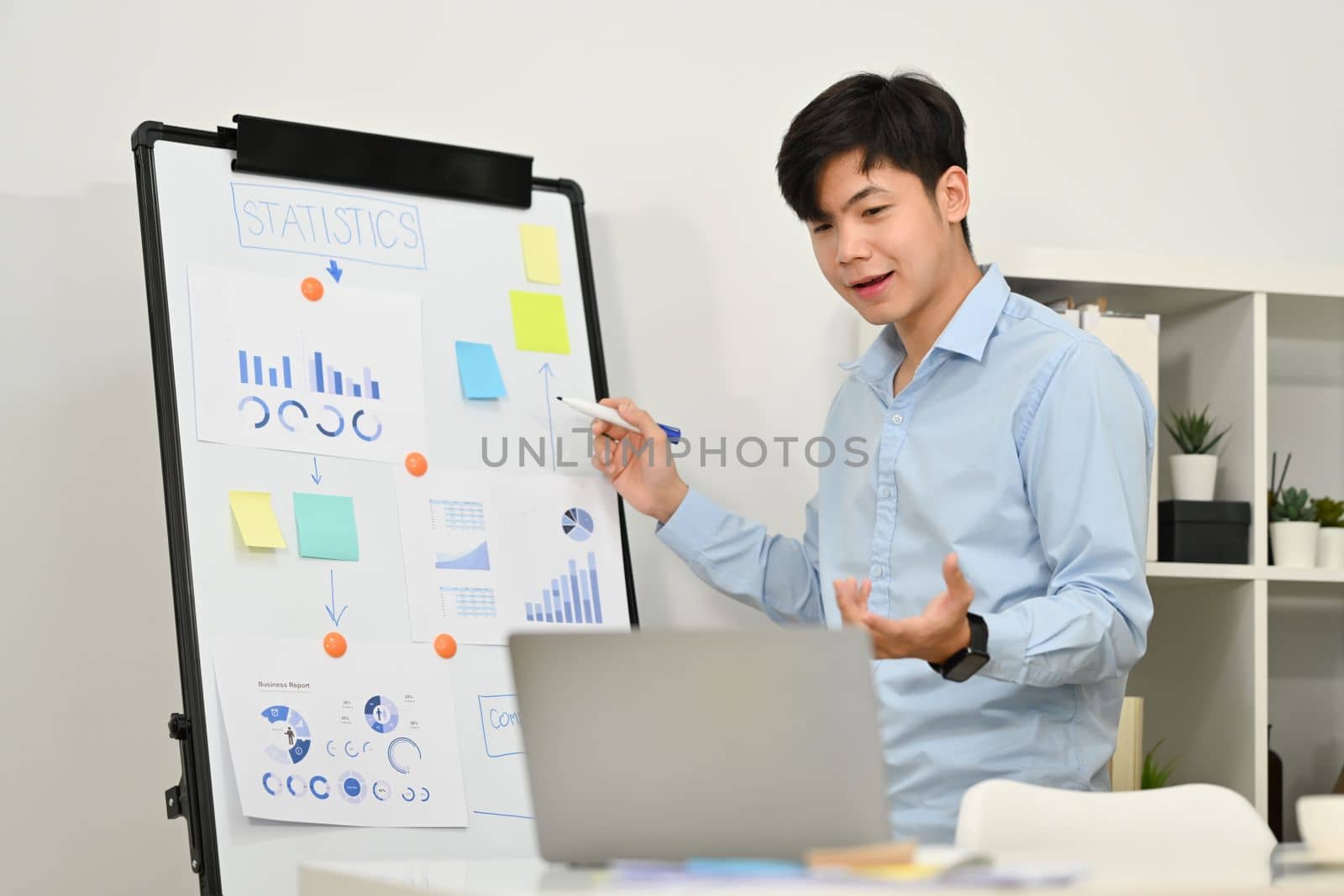 Confident businessman explaining business data on whiteboard during online conference via laptop computer by prathanchorruangsak