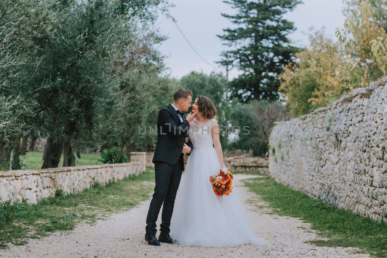 Happy stylish smiling couple walking in Tuscany, Italy on their wedding day. The bride and groom walk down the street by the hands. A stylish young couple walks. Husband and wife communicate nicely. Lovers run through the streets of the city.