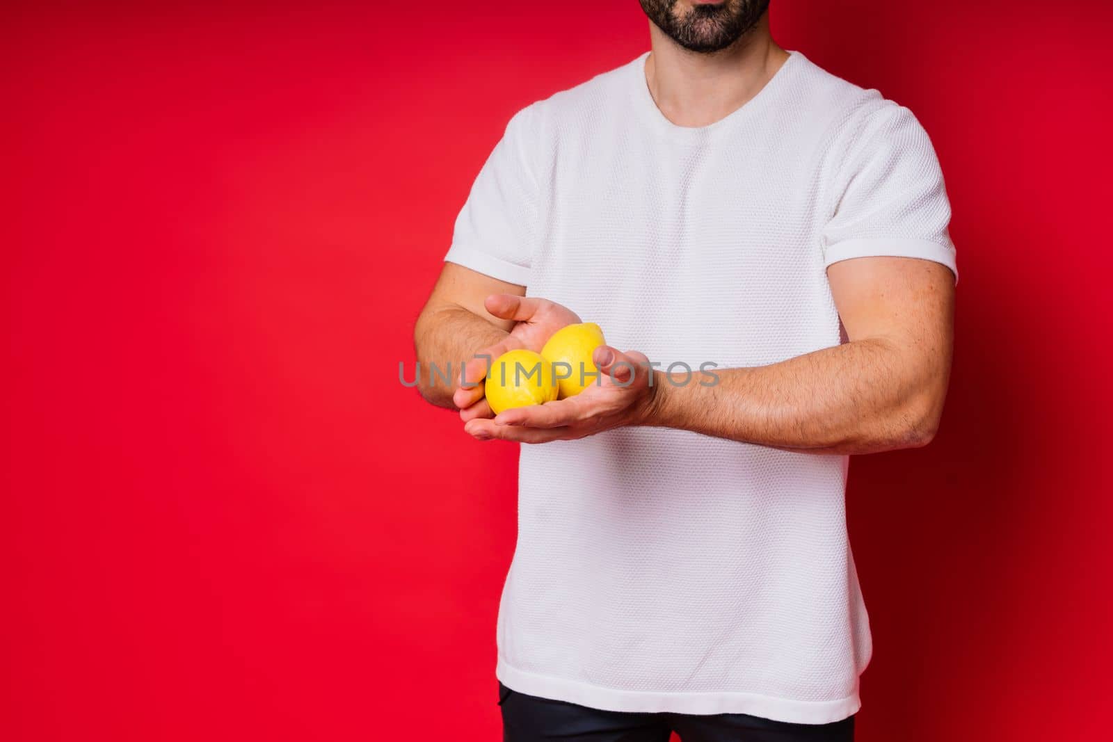 Portrait of young bearded man holding lemons in both hands on isolated red background by Zelenin