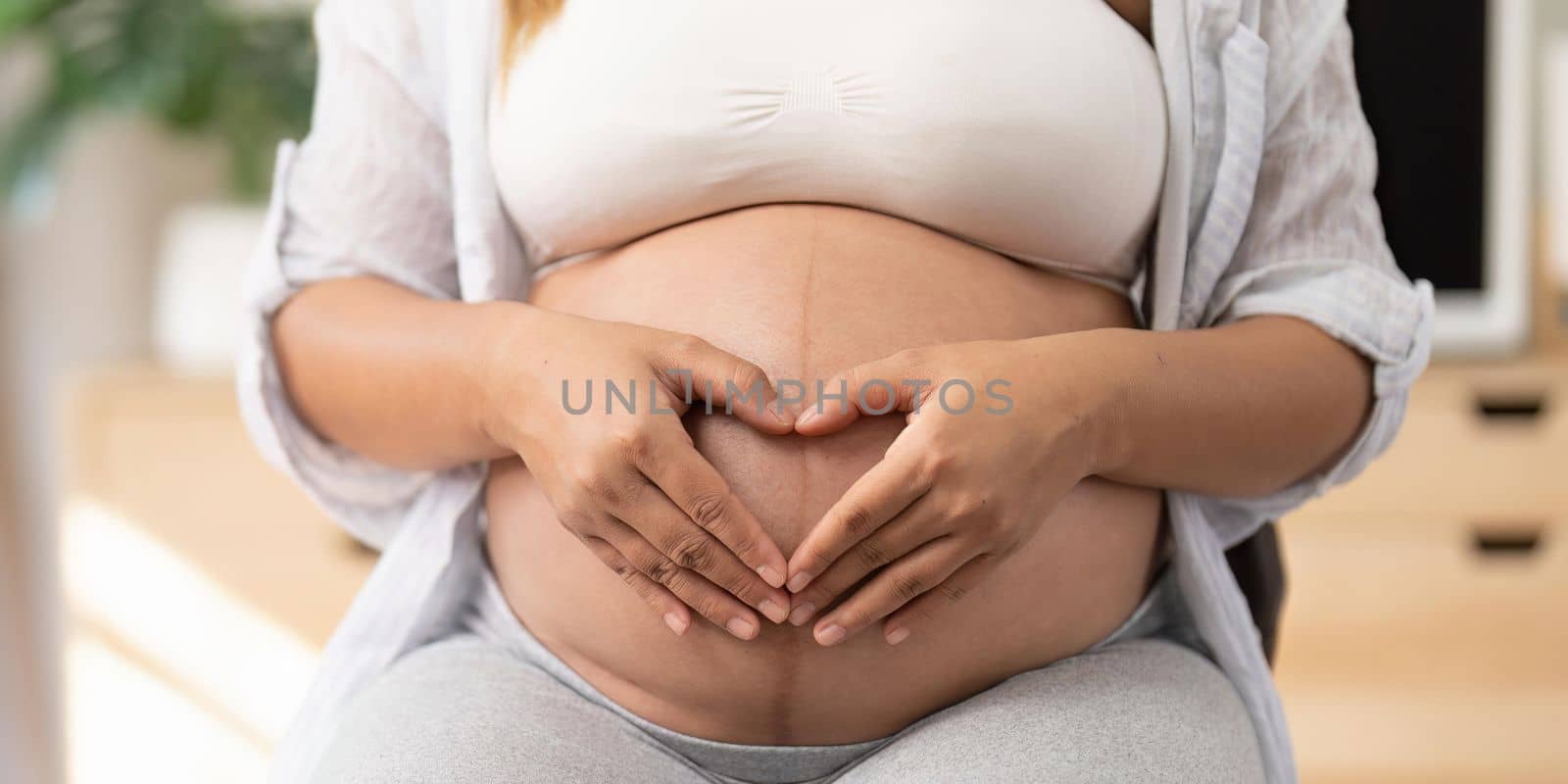 Pregnant woman holding hands on her belly making a heart symbol by nateemee